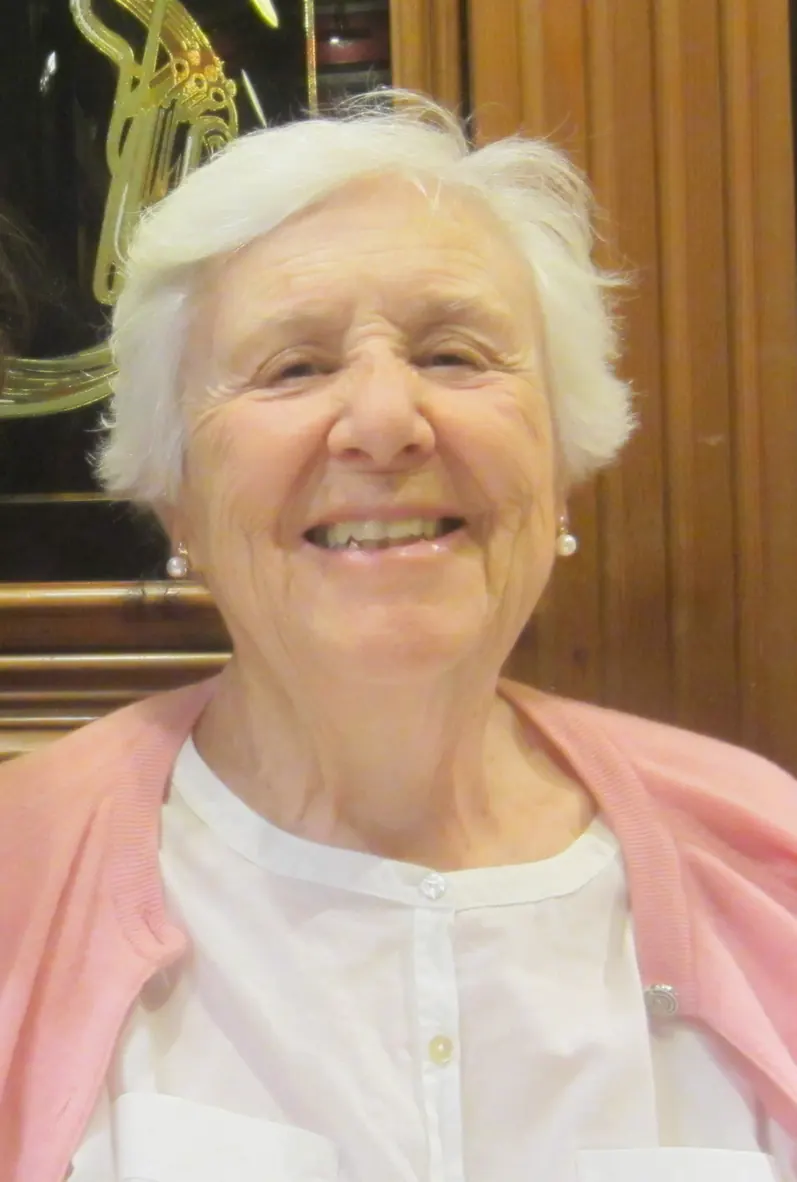 Una mujer mayor con el pelo blanco y corto sonrie en un despacho con paredes de madera